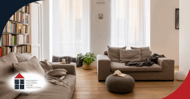 Cozy living room with neutral-toned sofas, bookshelf, and natural light from tall windows.