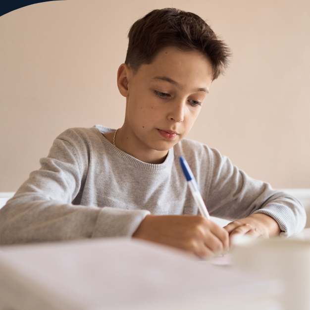 Focused boy writing at a desk in a bright room.