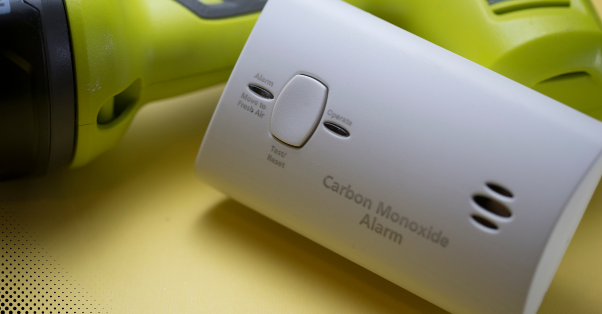 Close-up of a carbon monoxide alarm with a drill in the background.