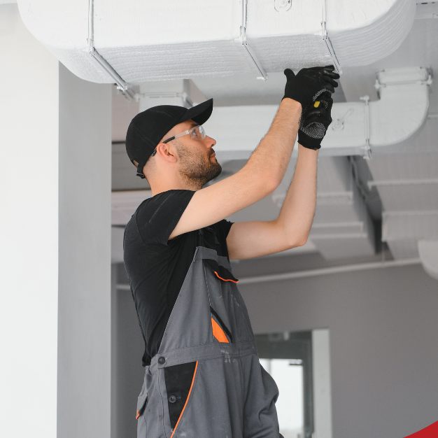 A worker inspecting ductwork in a ceiling.